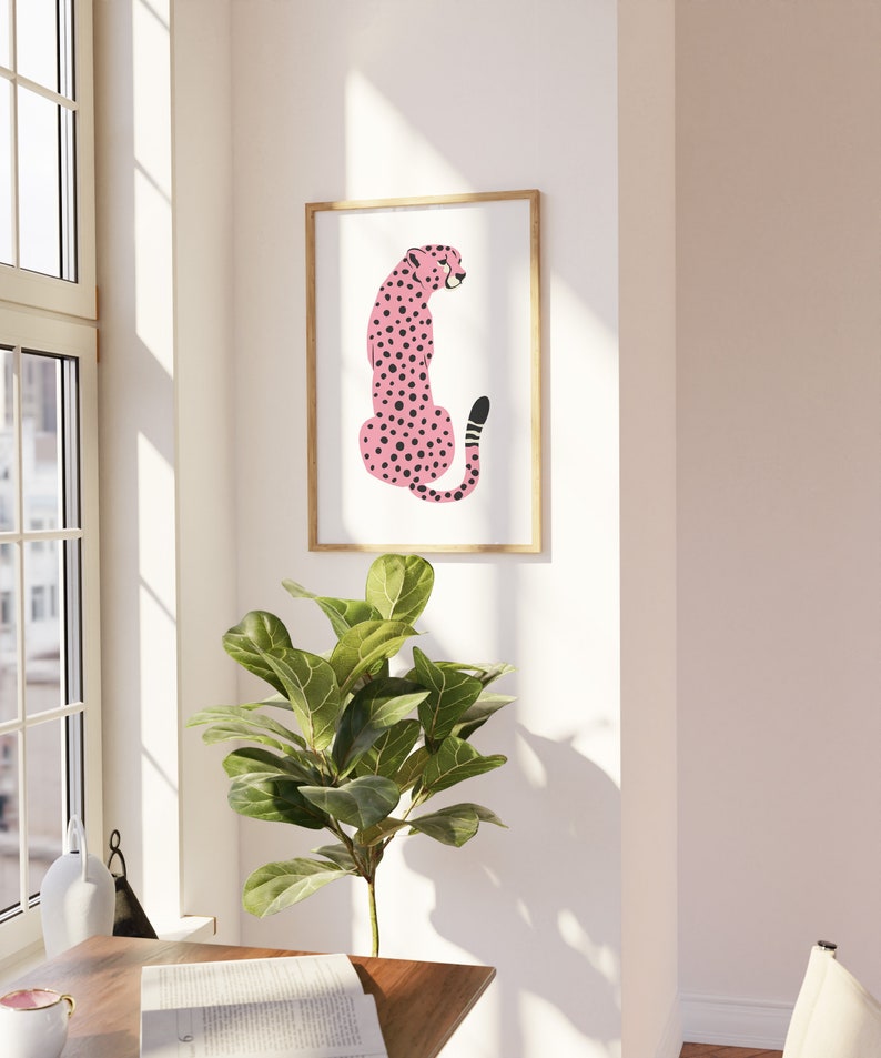 May include: A framed print of a pink cheetah with black spots sitting on a white background.