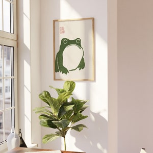 May include: A framed print of a green frog with a white background. The print has a red stamp in the top right corner.