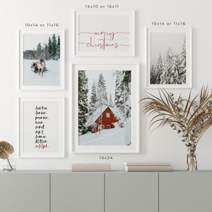 Op de afbeelding: Een set van vier witte ingelijste prints met winterse taferelen. De bovenste print zegt "vrolijk kerstfeest" in rode cursieve letters. De linker print heeft een zwart-wit foto van een rendier dat een slee trekt. De rechter print heeft een zwart-wit foto van een besneeuwd bos. De onderste print heeft een zwart-wit foto van een rood huisje in een besneeuwd bos. De prints zijn gerangschikt op een witte muur boven een grijze kast.