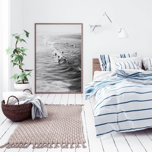 May include: A white bedroom with a bed with blue and white striped bedding. A black and white photograph of surfers hangs on the wall above the bed. A woven rug is on the floor in front of the bed.