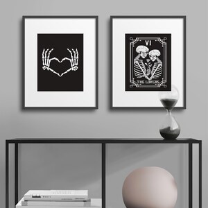 May include: Two black and white framed prints with skeleton imagery. The left print shows two skeletal hands forming a heart shape. The right print shows a tarot card with the number VI and the words "THE LOVERS" with two skeletons embracing.