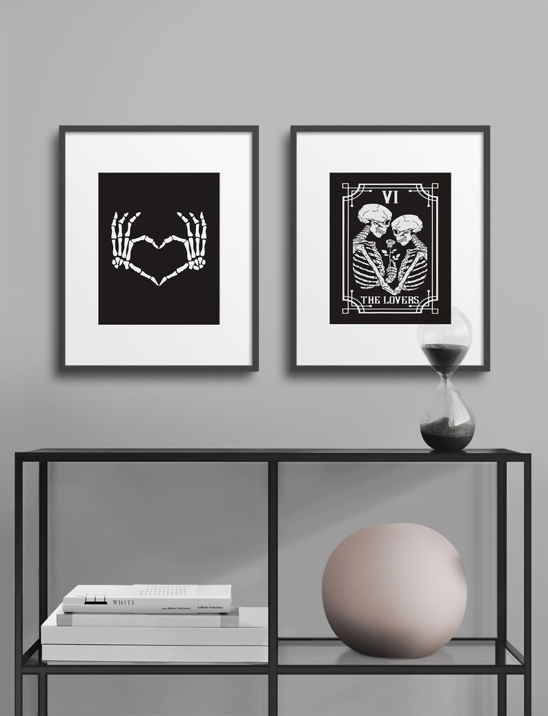 May include: Two black and white framed prints with skeleton imagery. The left print shows two skeletal hands forming a heart shape. The right print shows a tarot card with the number VI and the words "THE LOVERS" with two skeletons embracing.