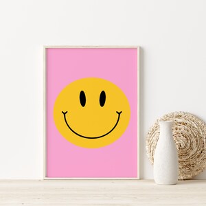 May include: A framed print with a yellow smiley face on a pink background.