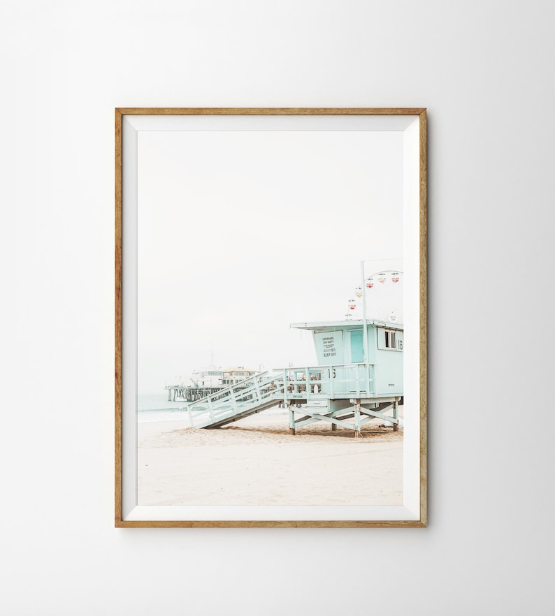 May include: A light blue lifeguard stand with a wooden ramp and stairs on a sandy beach. The stand has a sign that reads "Lifeguard Station 15". A pier is visible in the background.