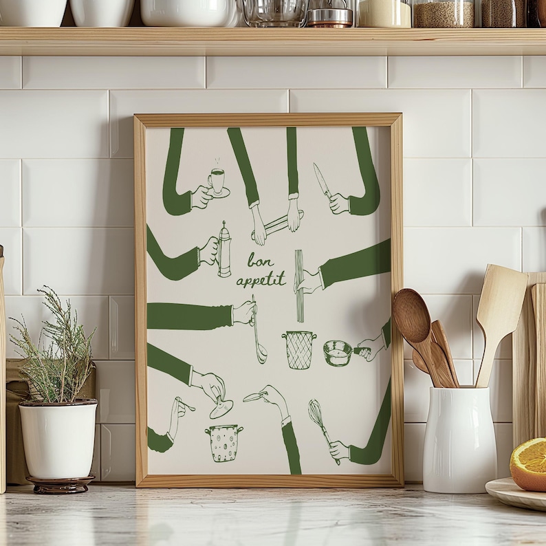 May include: A framed print with a white background and green illustrations of hands holding various kitchen utensils. The text "bon appetit" is written in the centre of the print.
