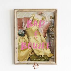 Puede incluir: Impresi&oacute;n enmarcada de estilo vintage que representa a una mujer con un vestido dorado, sentada sobre un coj&iacute;n rosa. Las palabras "BAD & BOUJEE" est&aacute;n escritas en rosa brillante sobre la imagen. La obra est&aacute; en un marco ornamentado y envejecido.
