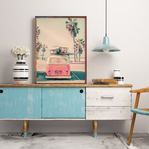 May include: A vintage pink Volkswagen van with surfboards on the roof parked in front of a beach scene with palm trees. The van has a license plate that says "SURF'S UP". The image is printed on a canvas and framed in a wooden frame.