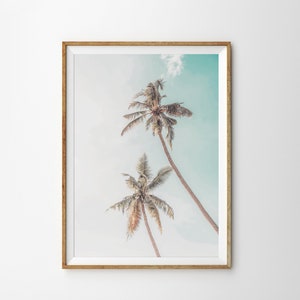 May include: A framed print of two palm trees against a light blue sky. The trees are silhouetted against the sky, with their fronds reaching up towards the top of the frame.