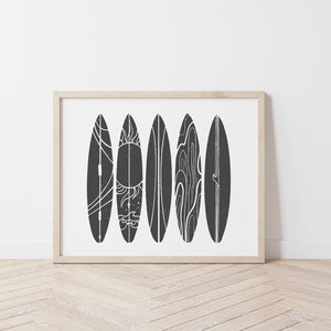 May include: A framed print of six black and white surfboards with different designs. The surfboards are arranged vertically in a row. The background is white.