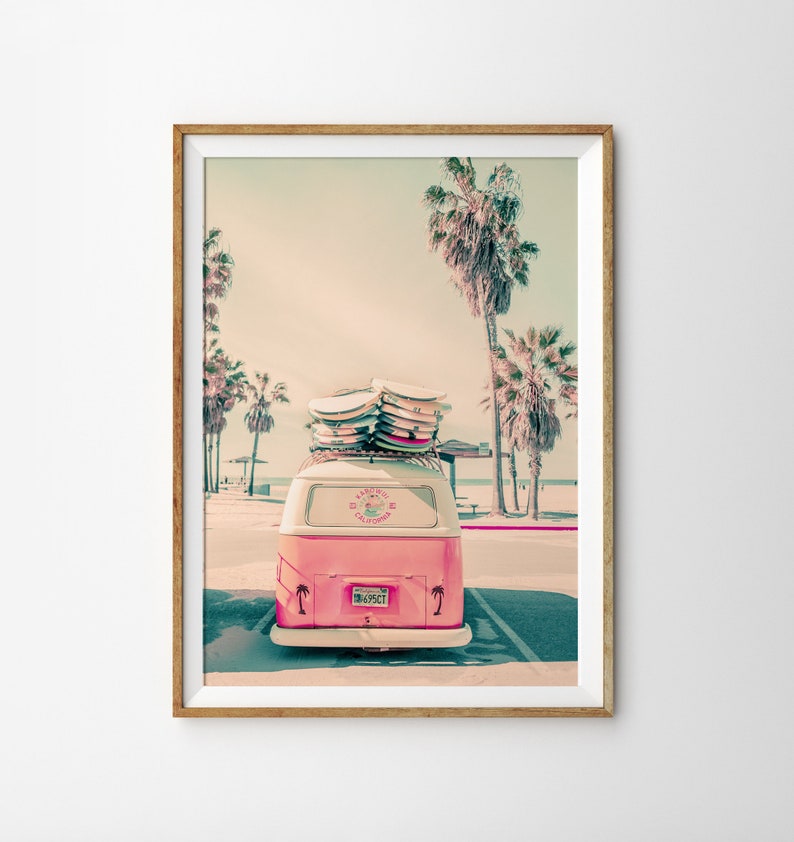 May include: A pink vintage van with surfboards on the roof parked in front of palm trees. The van has a sticker that says "California Surf Club".