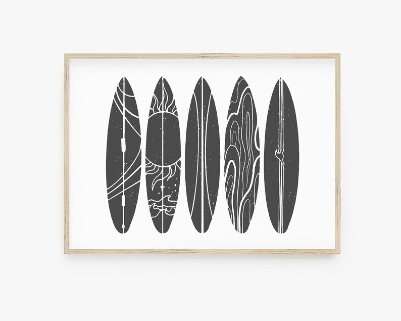 May include: A black and white print of five surfboards with different designs, including a sun, waves, and a line pattern. The surfboards are framed in a light wood frame.