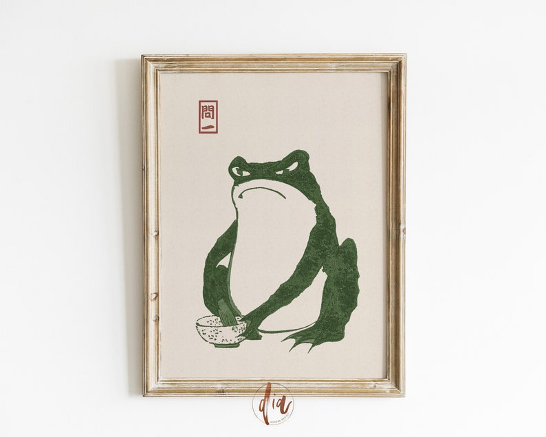 May include: A framed print of a green frog holding a bowl. The frog is sitting on a beige background with the Japanese character "開" in red.
