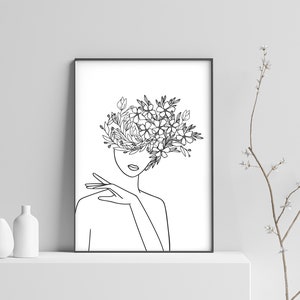 May include: Line art drawing of a person with flowers growing from their head. The drawing is in black and white and is framed in a black frame.