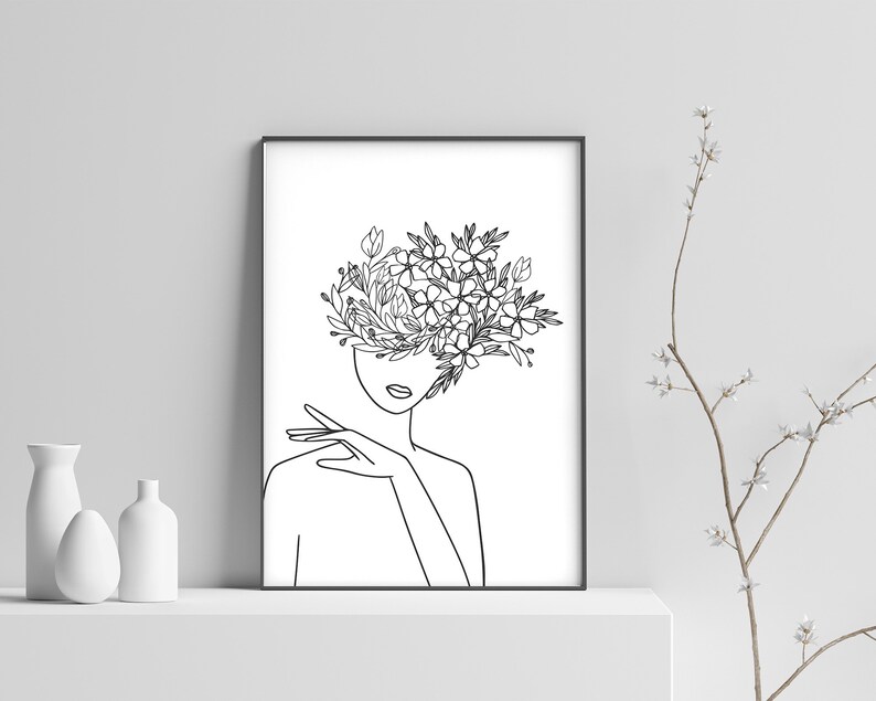 May include: Line art drawing of a person with flowers growing from their head. The drawing is in black and white and is framed in a black frame.