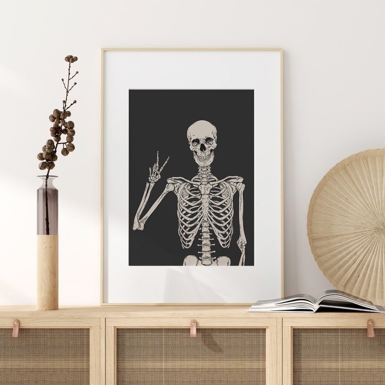 May include: A framed print of a skeleton with a skull making a peace sign. The skeleton is white and the background is black.