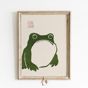 May include: A framed print of a green frog silhouette on a beige background. A red stamp with Japanese characters is in the top right corner.