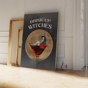 K&ouml;nnte beinhalten: Ein schwarzes und goldenes Poster mit dem Text "Drink Up Witches" und einer Hexe, die in einem Martini-Glas sitzt. Die Hexe tr&auml;gt einen schwarzen Hut und ein schwarzes Kleid und hat einen goldenen Heiligenschein.