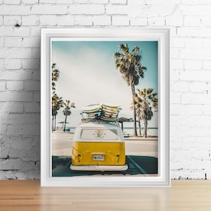 May include: A yellow vintage van with surfboards on the roof parked in front of a beach with palm trees. The van has a white stripe and the words "KAUAI SURF CLUB" on the back.