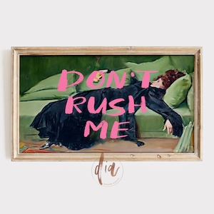 Può includere: Stampa incorniciata di un dipinto vintage raffigurante una persona in abito nero sdraiata su un divano verde. Le parole "DON'T RUSH ME" sono scritte in rosa acceso sull'immagine. L'opera d'arte ha una cornice color oro.