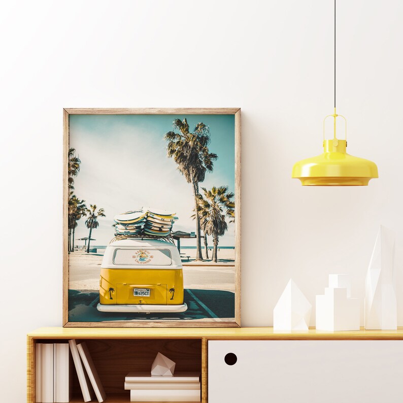 May include: A yellow and white vintage van with surfboards on the roof parked in front of a beach with palm trees. The van has a "Surf City" logo on the side and a California license plate.