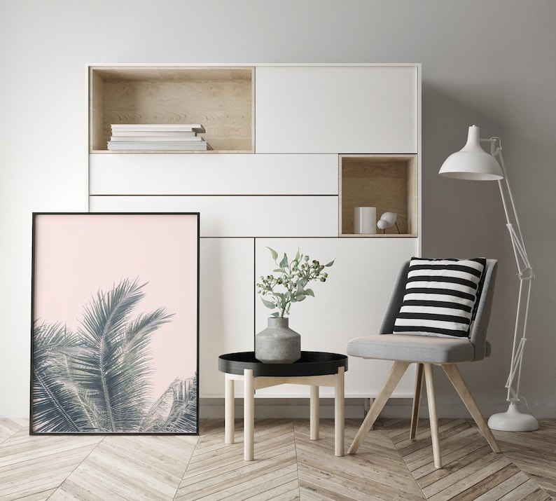 May include: A white shelf unit with a light wood interior, featuring a framed print of a palm tree against a pink background, a small potted plant, and a gray chair with a black and white striped cushion. The chair is positioned in front of a small wooden table.