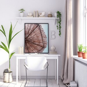 May include: A white desk with a white chair and a framed print of a beach umbrella. The desk has a shelf above it with decorative items, including books, a seashell, and a plant. There is a plant on the floor next to the desk and a window with curtains in the background.