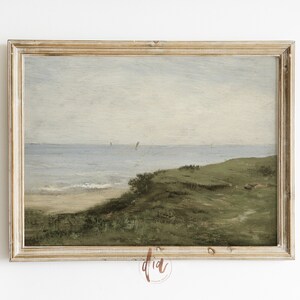 May include: A framed painting depicting a seascape with a grassy hill in the foreground, a sandy beach, and a blue ocean with a few sailboats in the distance. The sky is a light blue with some clouds.