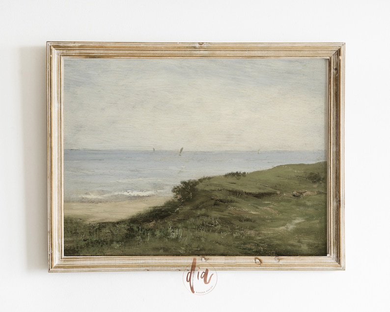 May include: A framed painting depicting a seascape with a grassy hill in the foreground, a sandy beach, and a blue ocean with a few sailboats in the distance. The sky is a light blue with some clouds.