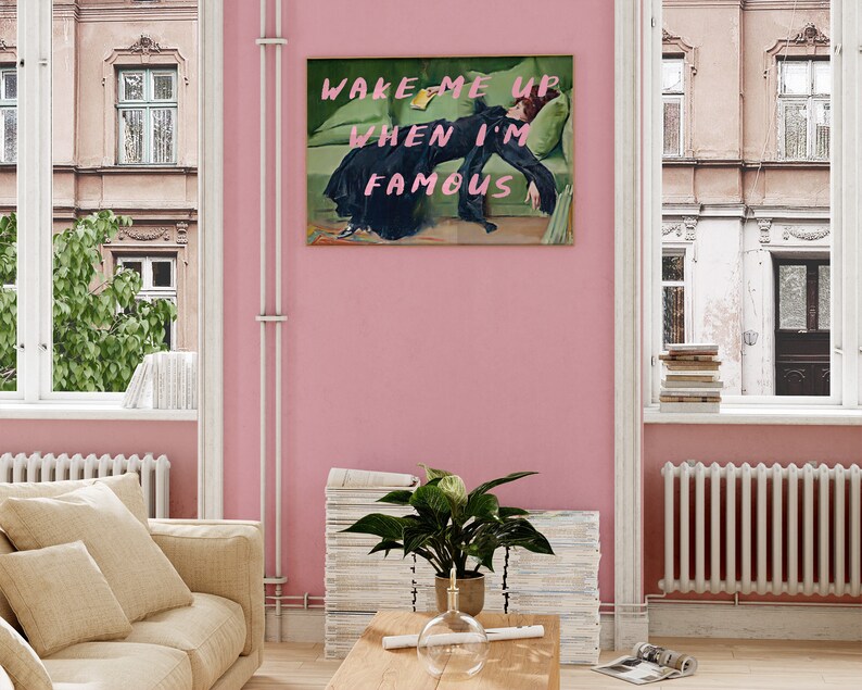 May include: A pink wall with a framed print of a woman lying on a green couch. The print says "WAKE ME UP WHEN I'M FAMOUS".