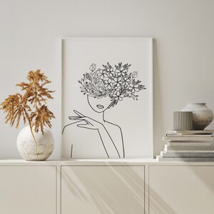 May include: A black and white line drawing of a person with flowers covering their face. The drawing is on a white background and is framed in a white frame.