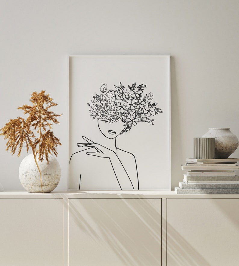 May include: A black and white line drawing of a person with flowers covering their face. The drawing is on a white background and is framed in a white frame.