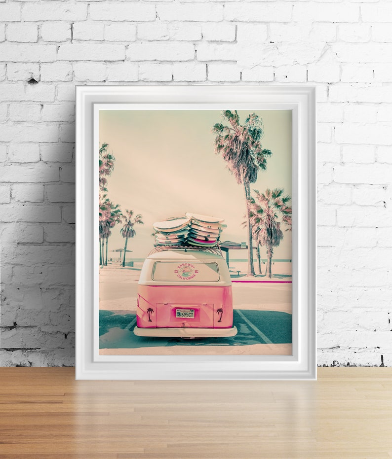 May include: A pink vintage van with surfboards on the roof parked in front of palm trees. The van has a sticker that says "Karni Surf California" and a license plate that says "TM 695CT".