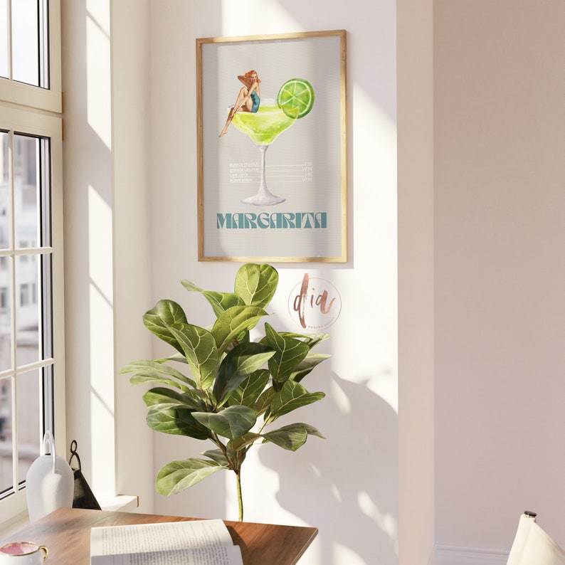May include: A watercolor illustration of a margarita cocktail with a woman sitting on the rim of the glass. The illustration is framed and has the word "Margarita" written below the glass.