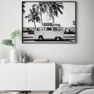 May include: Black and white photograph of a vintage white van with a surfboard on the roof driving down a palm tree lined street.