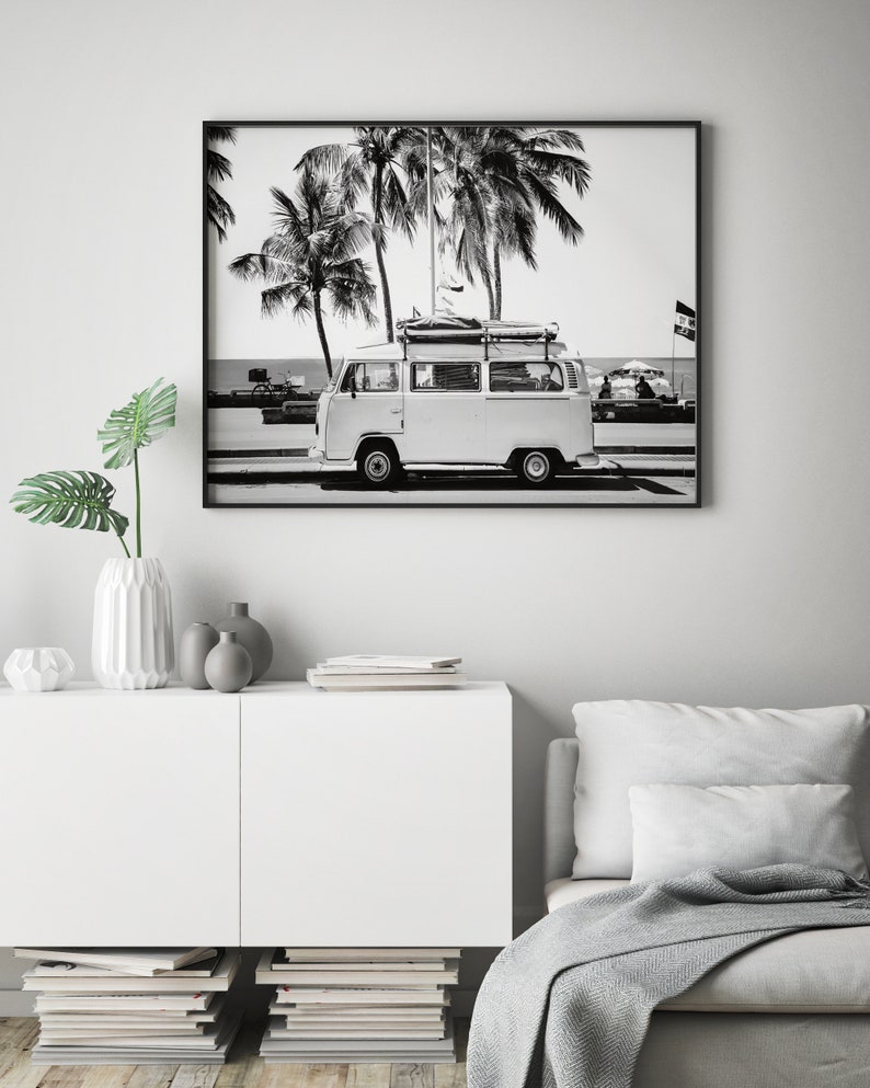 May include: Black and white photograph of a vintage white van with a surfboard on the roof driving down a palm tree lined street.
