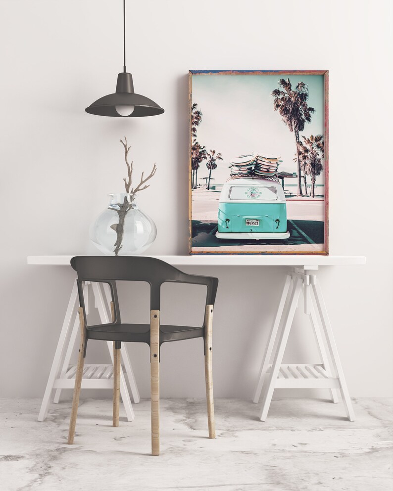 May include: A teal blue vintage van with surfboards on the roof parked in front of palm trees. The van has a license plate that reads "SURF 67". The image is framed in a wooden frame.