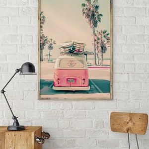 May include: A pink vintage van with surfboards on the roof parked in front of a beach with palm trees. The van has a license plate that reads "843527".