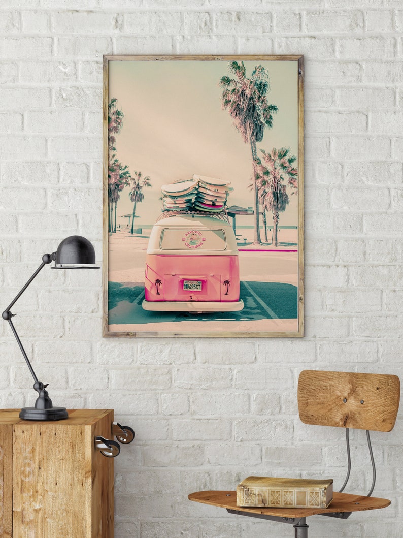 May include: A pink vintage van with surfboards on the roof parked in front of a beach with palm trees. The van has a license plate that reads "843527".