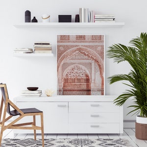 May include: A white shelf with books and decorative objects, a white dresser with drawers, a black chair, a potted plant, and a framed print of a red archway with intricate details.