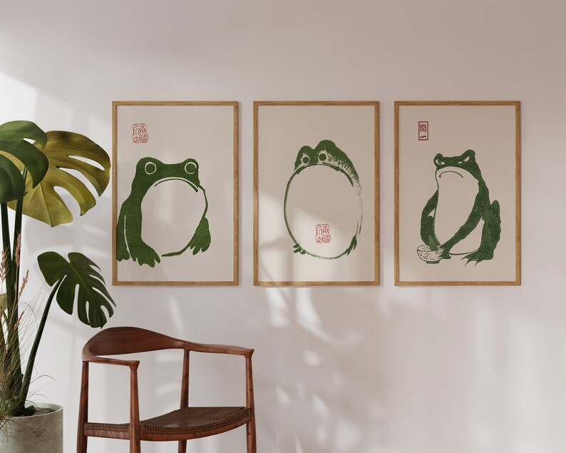 May include: Three framed prints of green frogs on a white background. The frogs are in different poses, one is sitting, one is standing, and one is holding a bowl. The prints are in wooden frames.