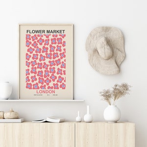 Pu&ograve; includere: Una stampa incorniciata con un motivo floreale rosa e blu e il testo "FLOWER MARKET LONDON" in nero. La stampa &egrave; appesa a una parete bianca sopra uno scaffale in legno con un vaso bianco, un piccolo vaso bianco e una zucca marrone.
