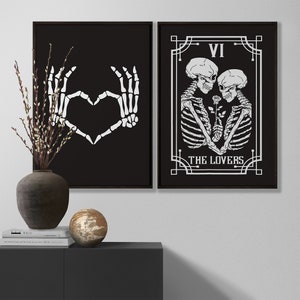 May include: Two black framed prints with white illustrations. The left print shows two skeletal hands forming a heart shape. The right print shows a tarot card with the number VI and the words "THE LOVERS" with two skeletons embracing.