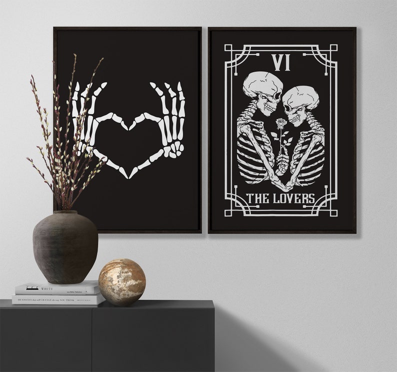 May include: Two black framed prints with white illustrations. The left print shows two skeletal hands forming a heart shape. The right print shows a tarot card with the number VI and the words "THE LOVERS" with two skeletons embracing.