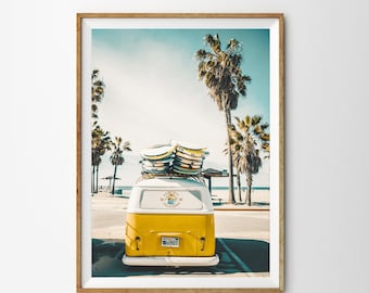 May include: A yellow vintage van with surfboards on the roof parked in front of a beach with palm trees. The van has a white stripe and a sticker that says "Santa Cruz California".