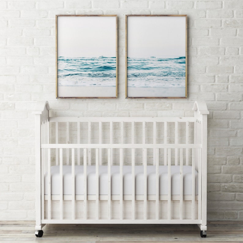 May include: Two framed photographs of ocean waves hanging above a white crib with a white mattress.