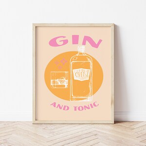 May include: A framed print with a yellow and orange background and pink text that reads "GIN AND TONIC". A white outline of a bottle of gin and a glass of gin and ice are in the center of the print.