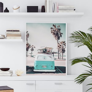 May include: A teal blue vintage van with surfboards on the roof parked in front of a beach with palm trees. The van has a license plate that reads "1869CT".