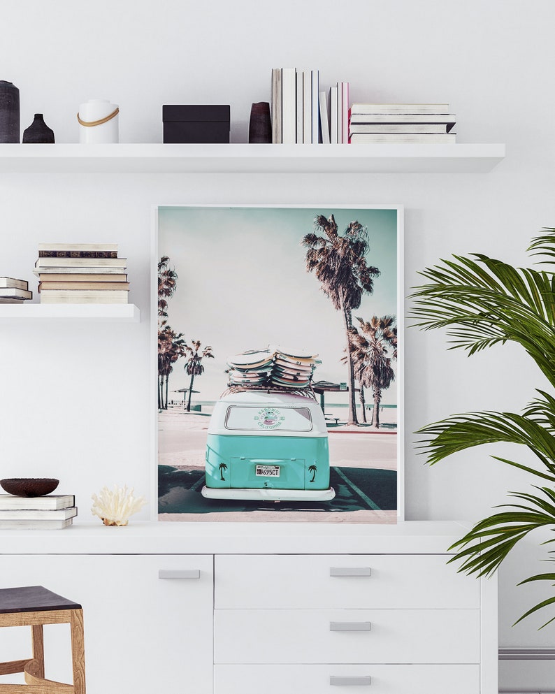 May include: A teal blue vintage van with surfboards on the roof parked in front of a beach with palm trees. The van has a license plate that reads "1869CT".