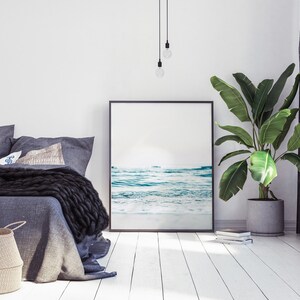Peut inclure: Int&eacute;rieur d'une chambre &agrave; coucher avec un lit, une photo encadr&eacute;e en noir d'une sc&egrave;ne de plage, une plante en pot et un luminaire suspendu.