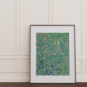 Op de afbeelding: Een ingelijste print van een schilderij dat een veld met bloemen in tinten roze, wit en paars toont. De bloemen worden omringd door groen gebladerte en de achtergrond is lichtblauw.